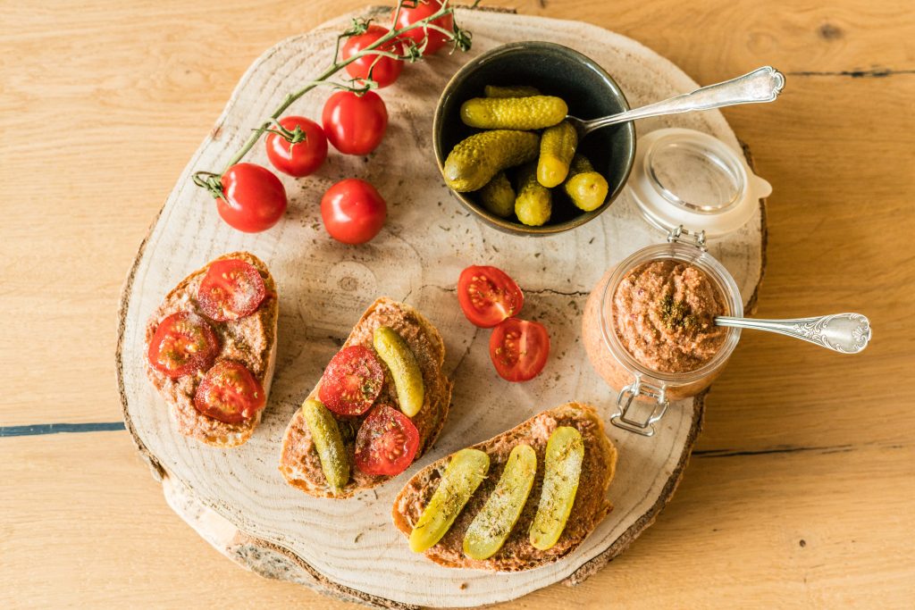 proteinreicher Brotaufstrich, angerichtet auf Baumscheibe, mit Brot, Tomaten und eingelegten Gurken