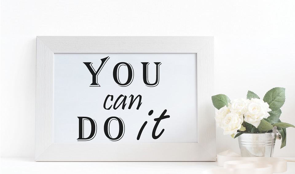 Spruch "You can do it" in weißem Bilderrahmen, vor weißem Hintergrund, neben Blume mit weißen Blüten