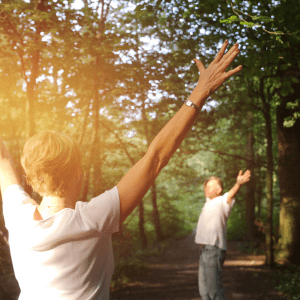 Zwei Menschen im Wald, mit weißem T-Shirt, die Arme gen Himmel gestreckt, die Sonne genießend