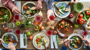 Ein bunt gedeckter Tisch mit Köstlichkeiten und essenden Menschen, von denen man nur die Hände sieht
